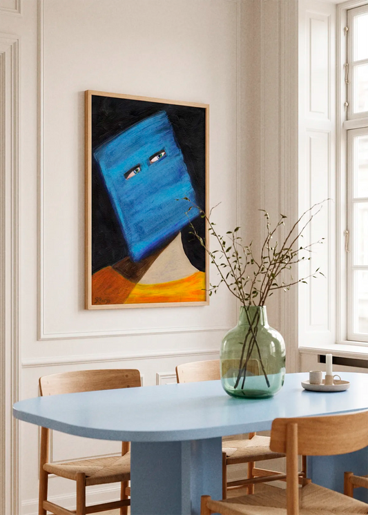 Abstract Blue Head Portrait by Sharyn Bursic displayed in a natural wood frame on a light wall above a blue dining table, styled with wooden chairs and a large glass vase in a bright modern interior.