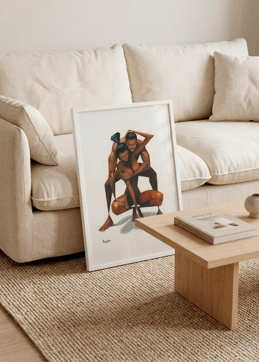 Abstract Loving Couple by Manasseh Johnson Sr. art print featuring two intertwined figures with geometric black shapes, displayed in a white frame leaning against a cream sofa in a warm Scandinavian living room.
