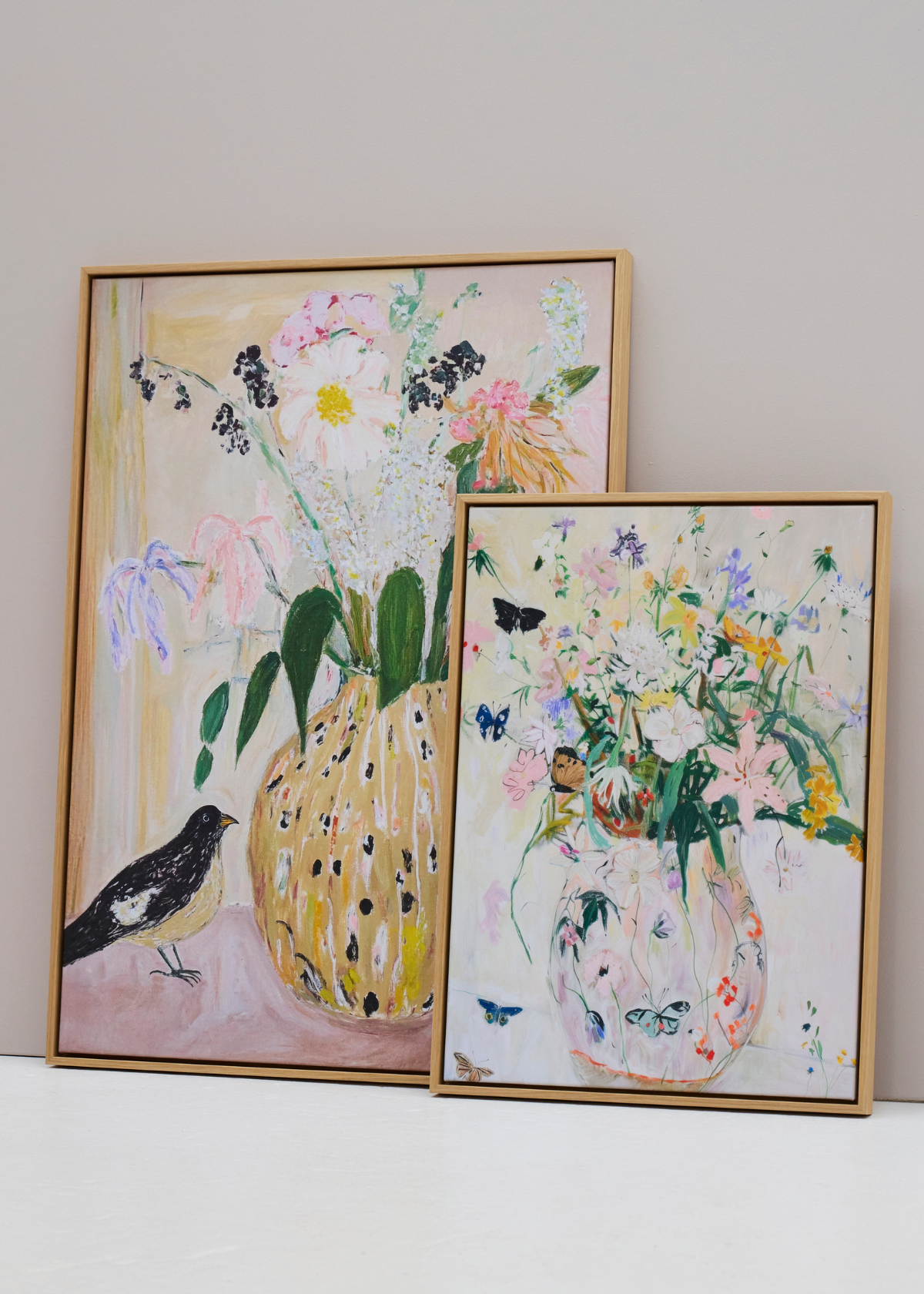 To farverige lærredstryk med blomster og fugle – Bird no. 2 og Wild Garden – i egetræsrammer, lænet op ad en lys væg.
