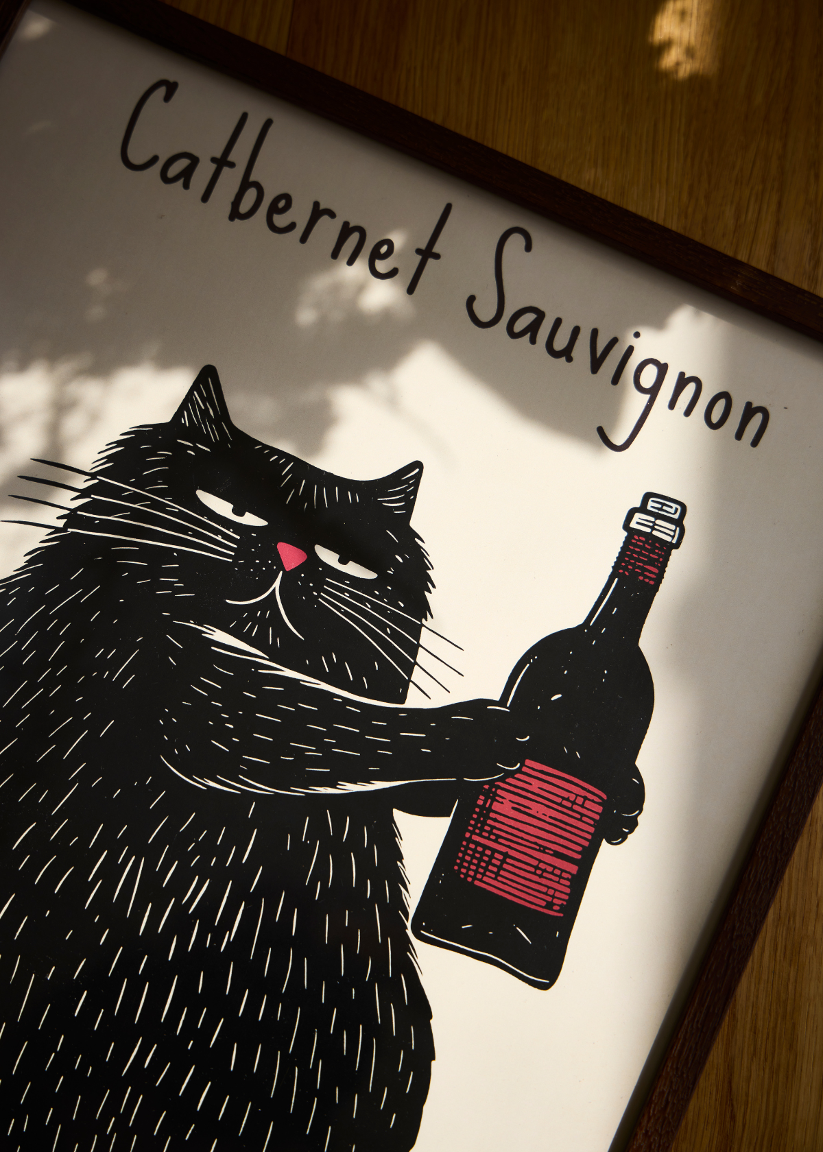 Plakaten Catbernet Sauvignon med en sort kat og en vinflaske, set i varme skygger på trægulv.