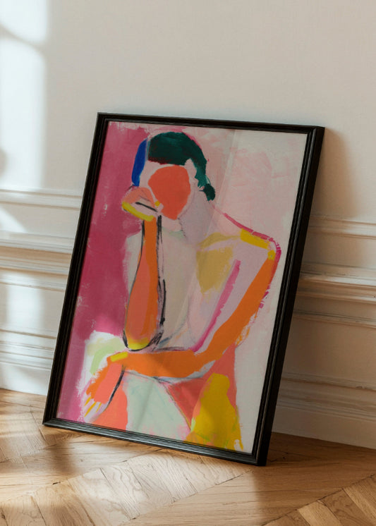 The Feminine poster showcasing vibrant, abstract brushstrokes in bold pink, orange, and yellow hues with accents of blue and green. Framed in sleek black, the artwork leans gracefully against a white paneled wall, casting soft shadows on the parquet floor, adding a contemporary and artistic flair to the space