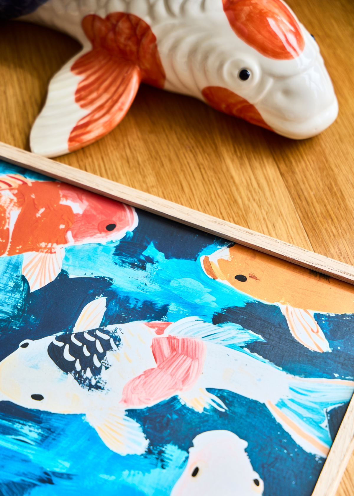 Farverig detalje af plakaten Koi med japanske fisk i blå, orange og hvide nuancer – liggende ved siden af en keramisk fisk.