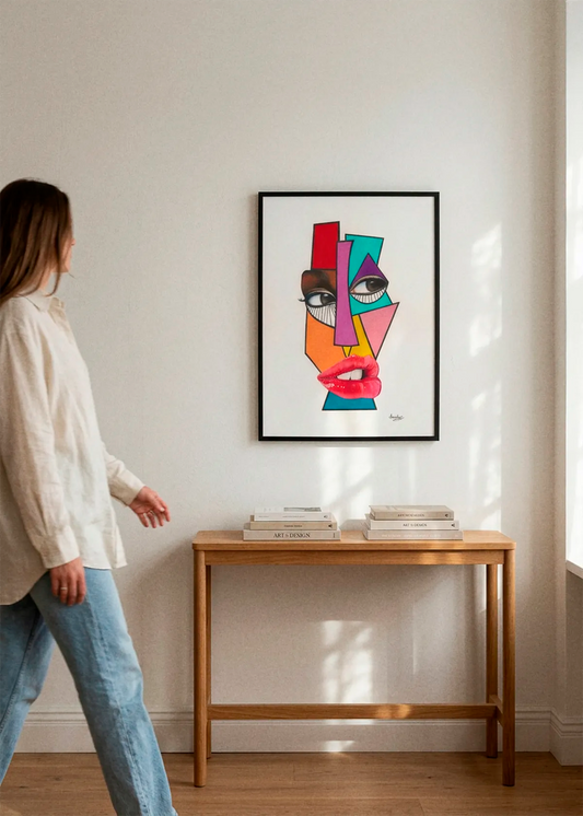 Vibrant Cubist Face by Manasseh Johnson Sr. art print featuring a bold abstract face with geometric shapes in red, pink, teal, orange and purple, displayed in a black frame above a wooden console in a bright Scandinavian interior.