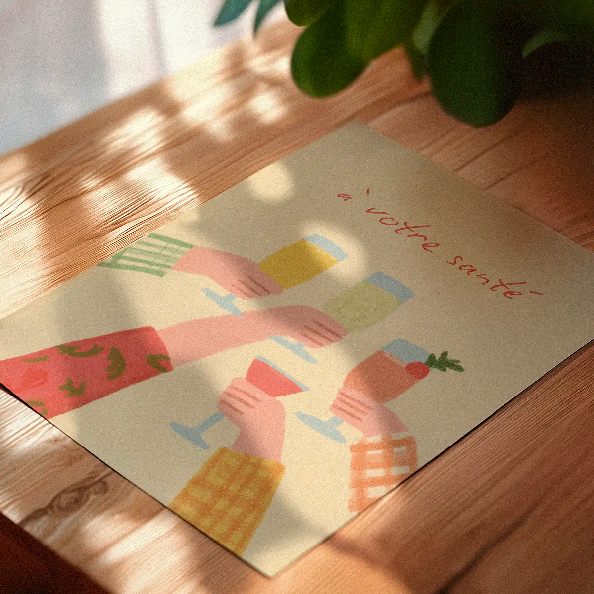 À votre santé poster with raised glasses in soft pastel colours, photographed on a wooden table with warm daylight and shadows.