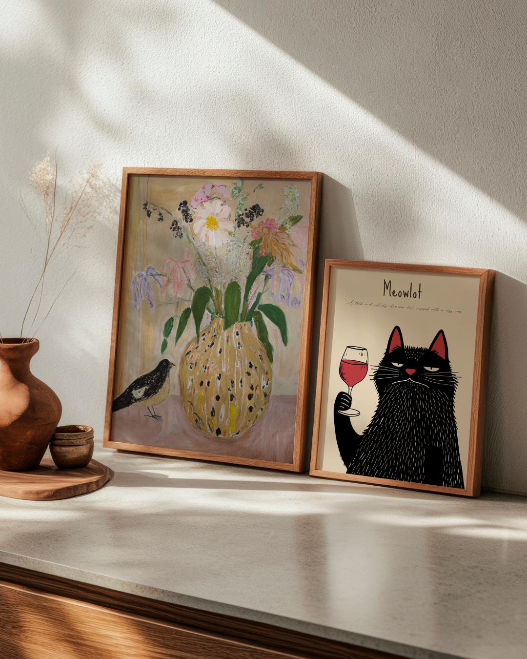 Contrasting HelloPoster prints: 'Bird no. 2', a soft floral still life, and 'Meowlot', a playful wine-loving black cat. Perfect for combining elegance and humor in your kitchen or hallway.