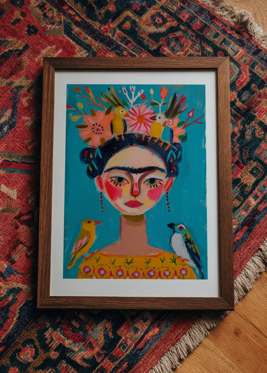 Colorful Frida Kahlo-inspired art print with birds and flowers in a wooden frame, styled on a patterned rug for a bohemian interior look.