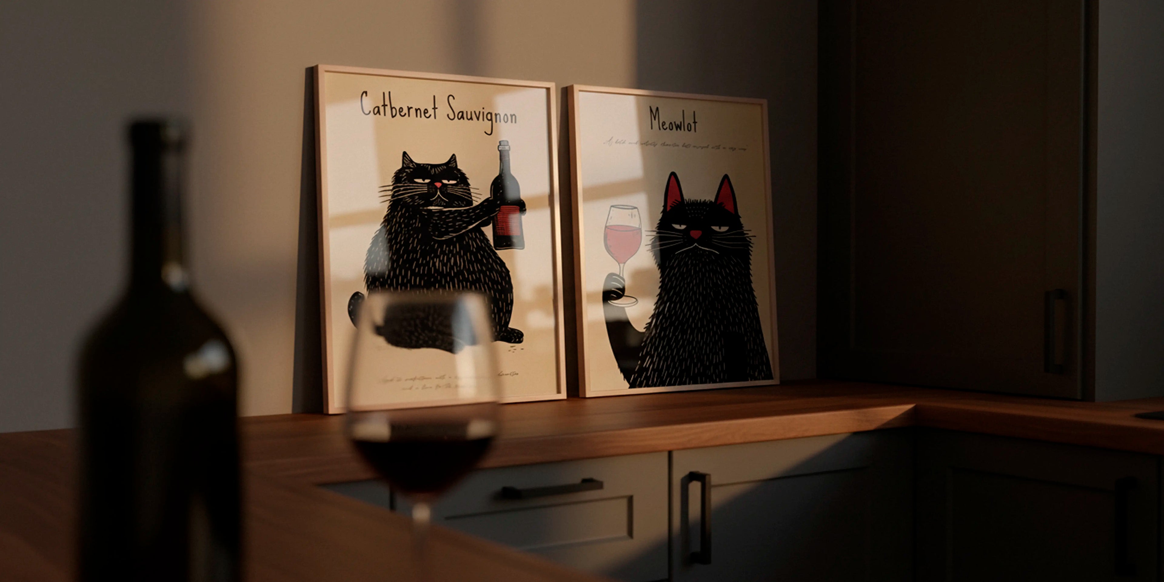 Two wine-themed cat posters — Catbernet Sauvignon and Meowlot — displayed on a kitchen counter in warm evening light, with a wine bottle and glass in the foreground.