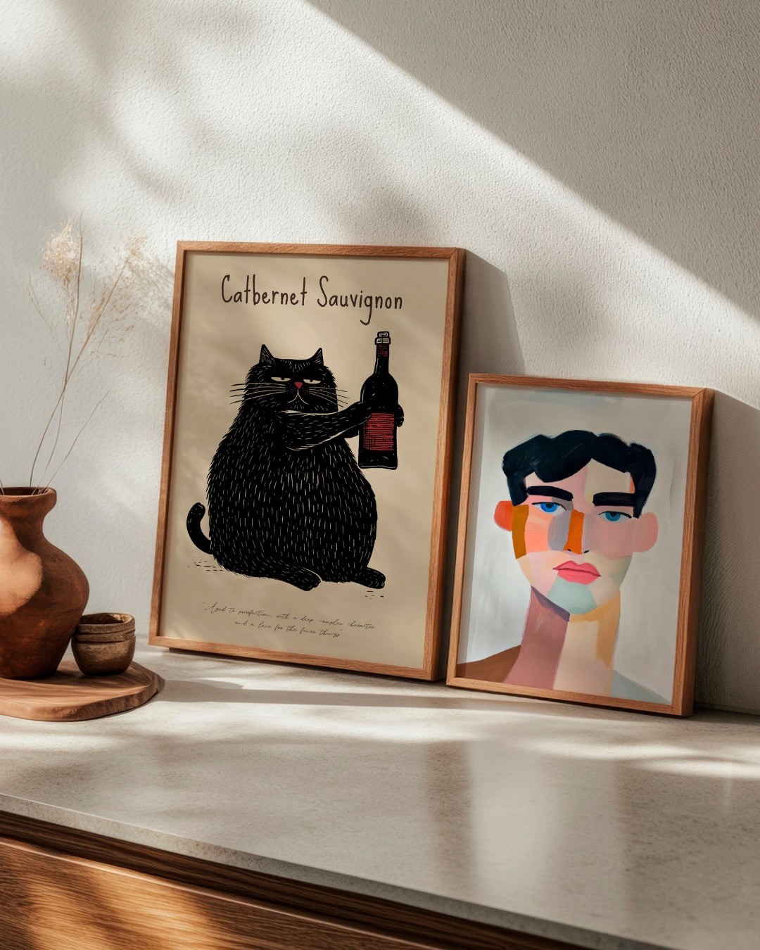 Modern poster set from HelloPoster: 'Catbernet Sauvignon' featuring a wine-drinking cat, and 'Male', a colorful abstract portrait. Stylish wall art for eclectic or minimalistic homes.
