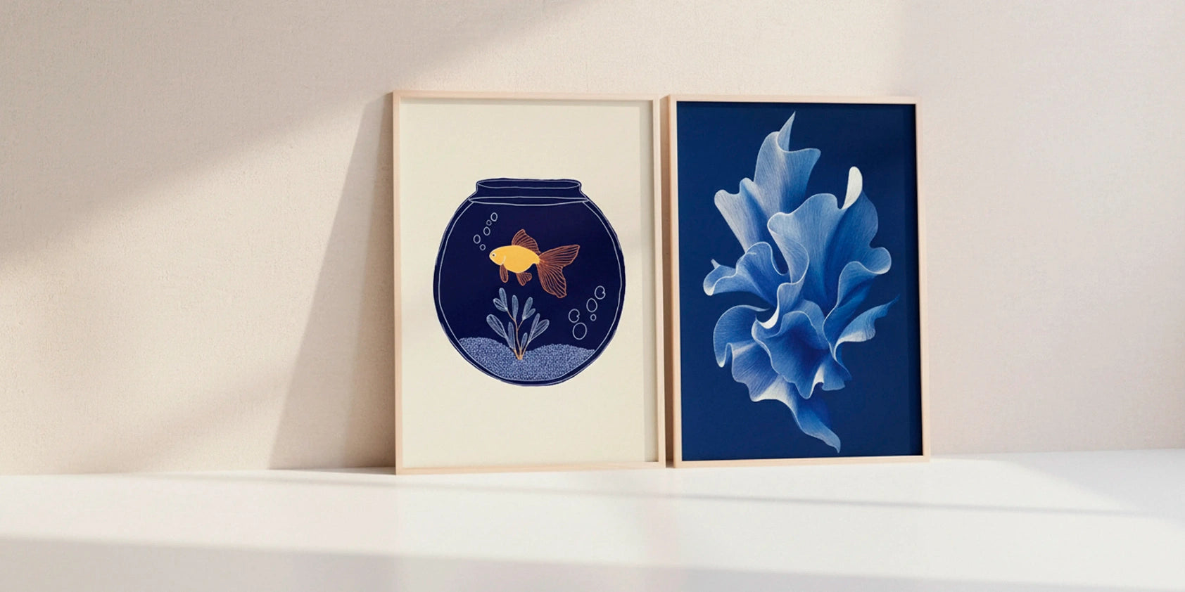 Fishy-shape no. 80 goldfish poster paired with a blue abstract floral artwork in oak frames on a bright sunlit wall in a Nordic interior.