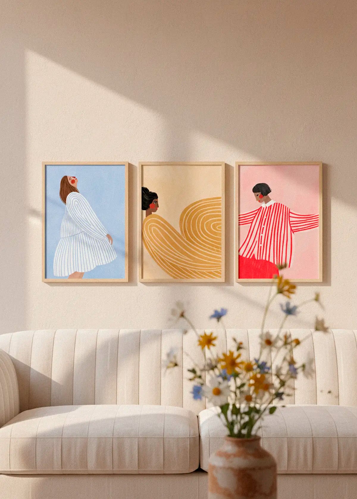 Gallery wall featuring Woman with the Blue Dress, Woman with the Yellow Dress and Woman with the Red Dress by Bea Muller styled above a light sofa in a calm Scandinavian living room