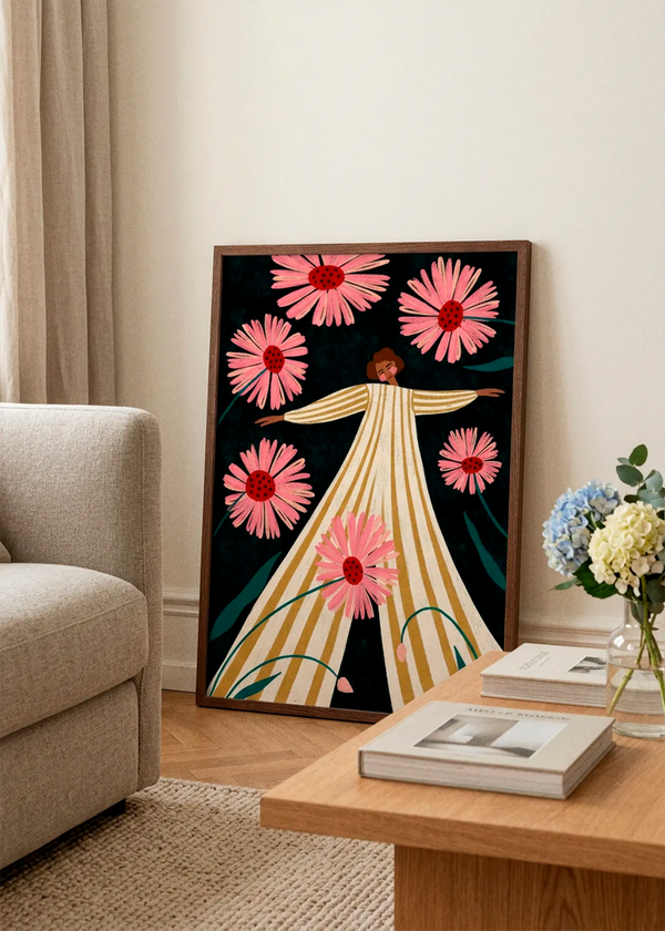 Joyful Woman In Bloom by Bea Müller displayed in a dark wood frame, leaning against a light wall beside a beige sofa and wooden coffee table in a soft, elegant living room.