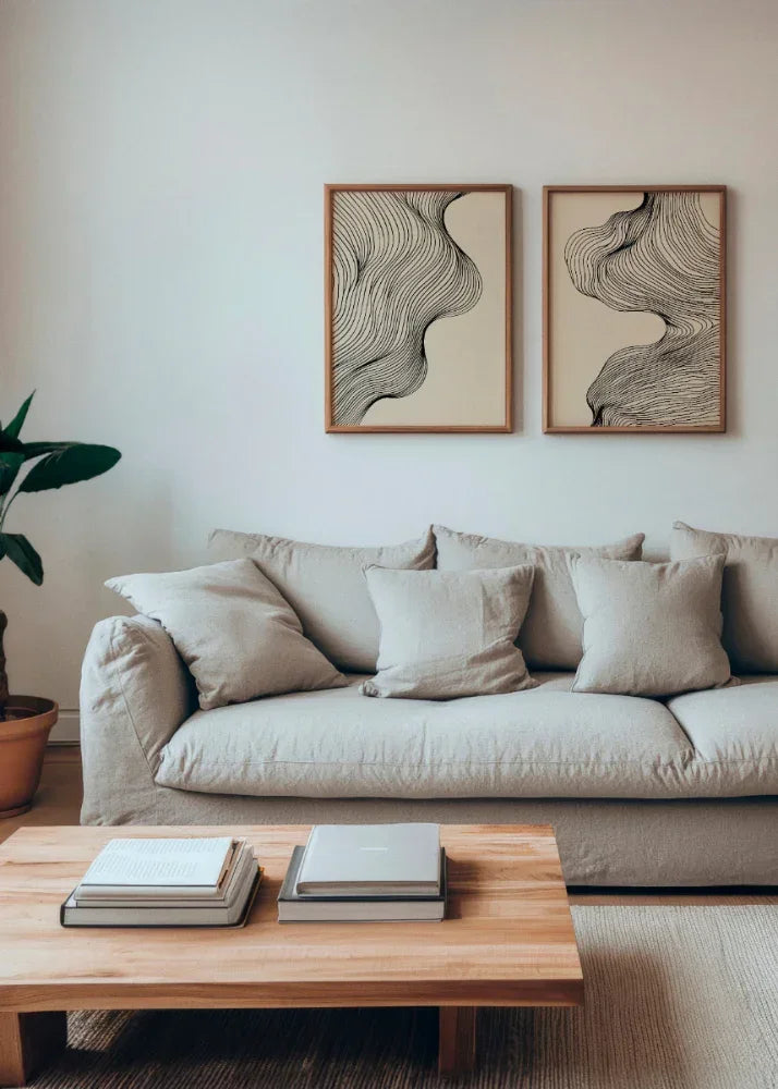 Miles and Tate posters featuring elegant black line art on a neutral beige background, framed in natural wood. The two artworks are displayed side by side above a cozy beige sofa, complemented by a wooden coffee table and a potted plant, creating a serene and minimalist living room ambiance.