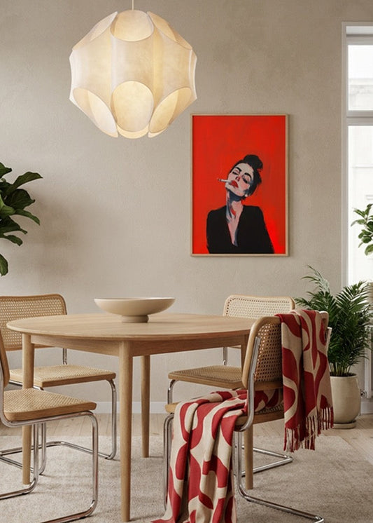RED poster with bold red background and expressive female portrait styled above round wooden dining table in modern Scandinavian interior.