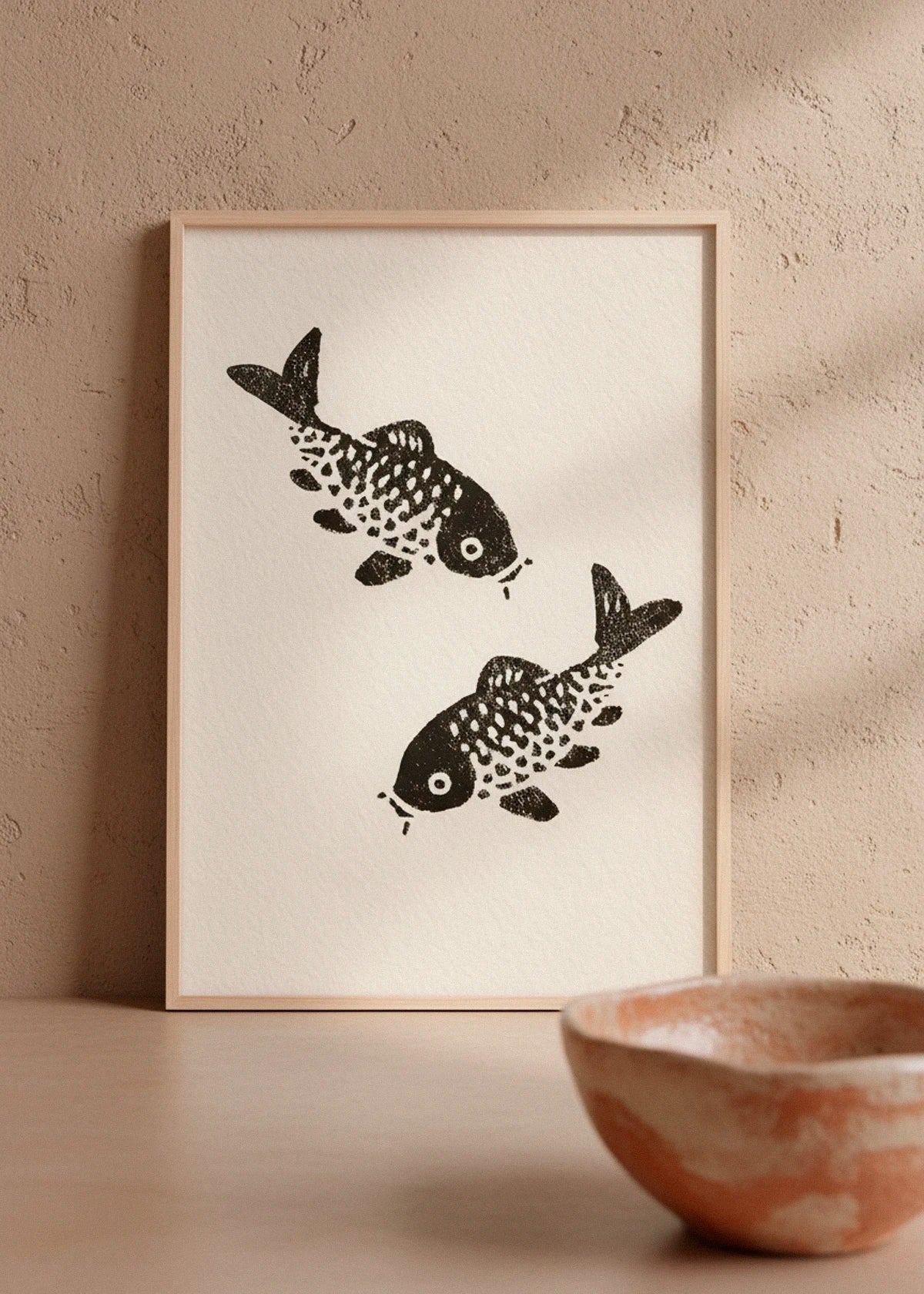 The Sakana poster with two black koi fish, standing against a textured beige wall with warm shadows.