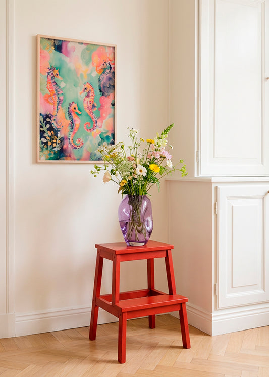 Sea World poster with colourful seahorses displayed in a bright Scandinavian interior, styled above a red wooden stool with a glass vase of fresh flowers, creating a calm and playful atmosphere.