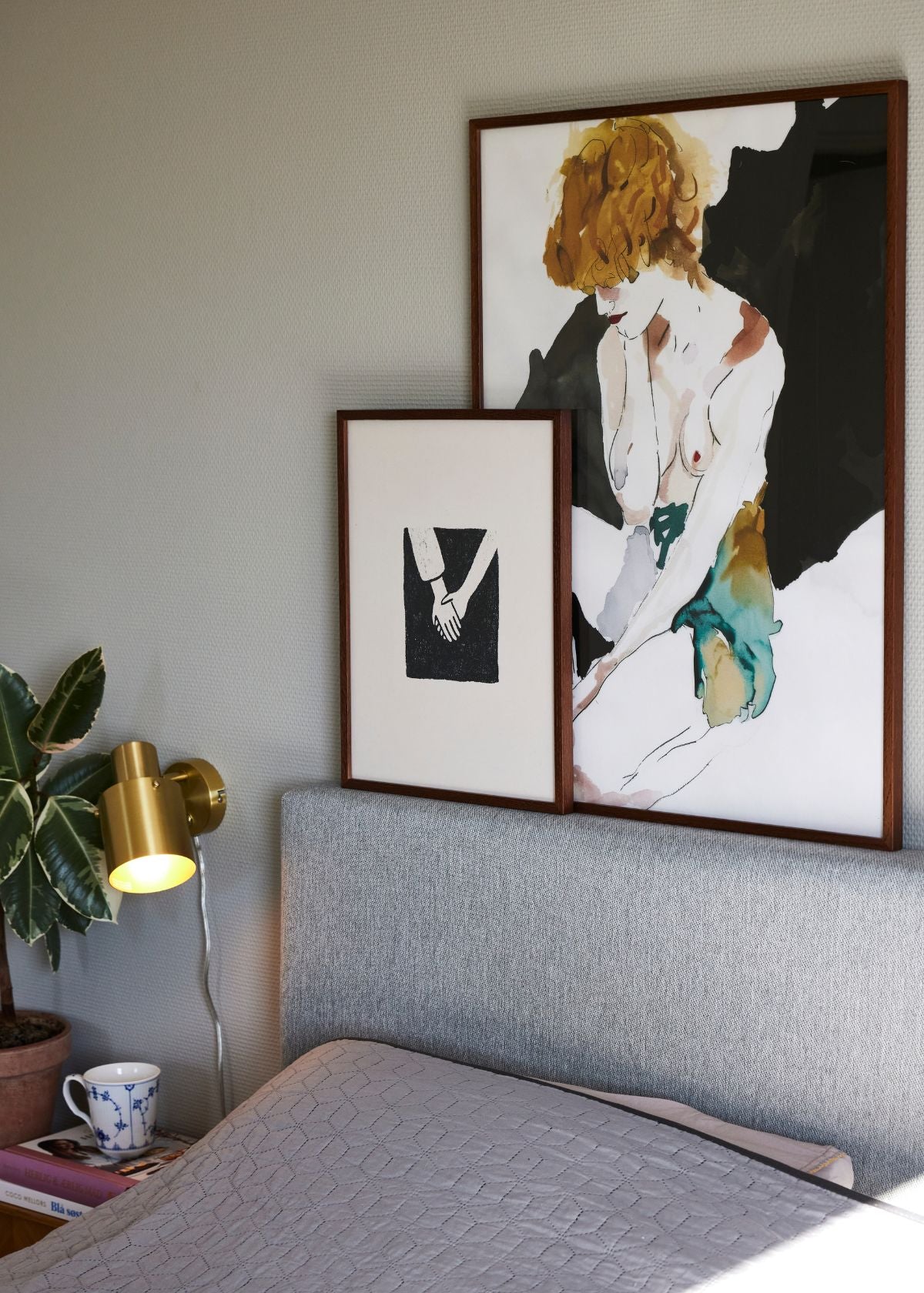 Togetherness and Femme Fatale posters styled together in wooden frames, adding contrast and personality to a Scandinavian bedroom interior.