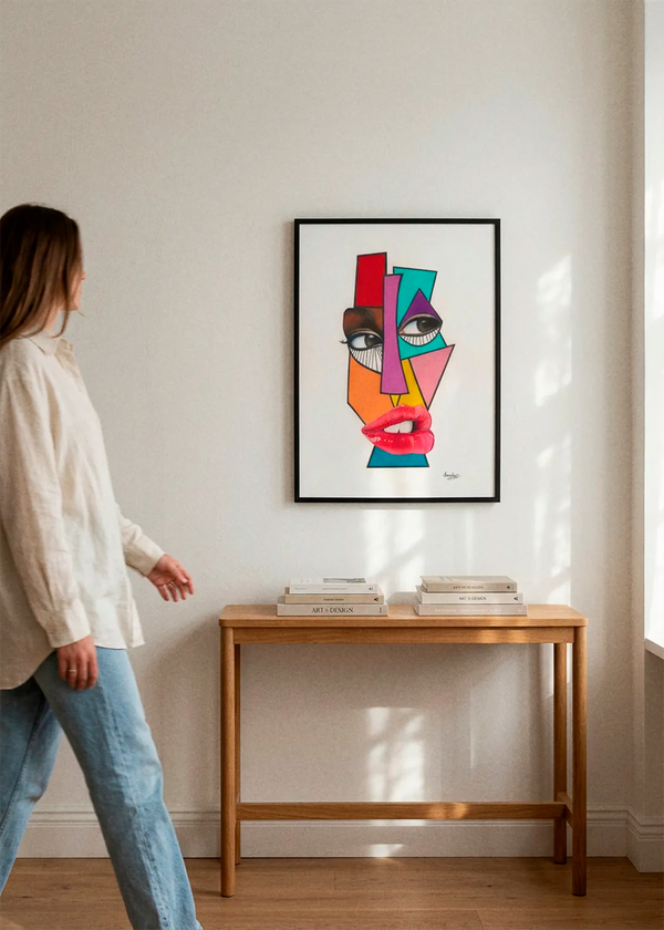 Vibrant Cubist Face by Manasseh Johnson Sr. art print featuring a bold abstract face with geometric shapes in red, pink, teal, orange and purple, displayed in a black frame above a wooden console in a bright Scandinavian interior.