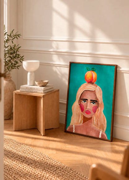 Woman With Peach plakat af Raissa Oltmanns i mørk træramme, stylet stående på gulvet i et lyst interiør med træmøbler og varme naturtoner.