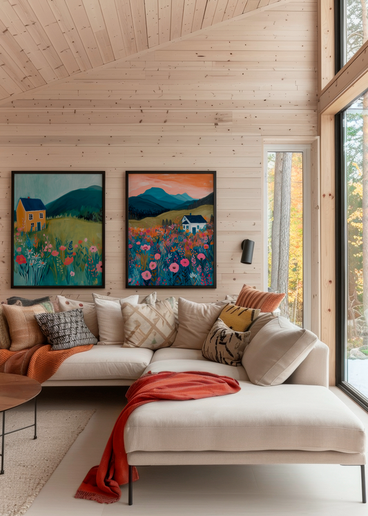 Two colorful landscape posters with houses and wildflowers hanging above a cozy sofa in a wooden cabin interior