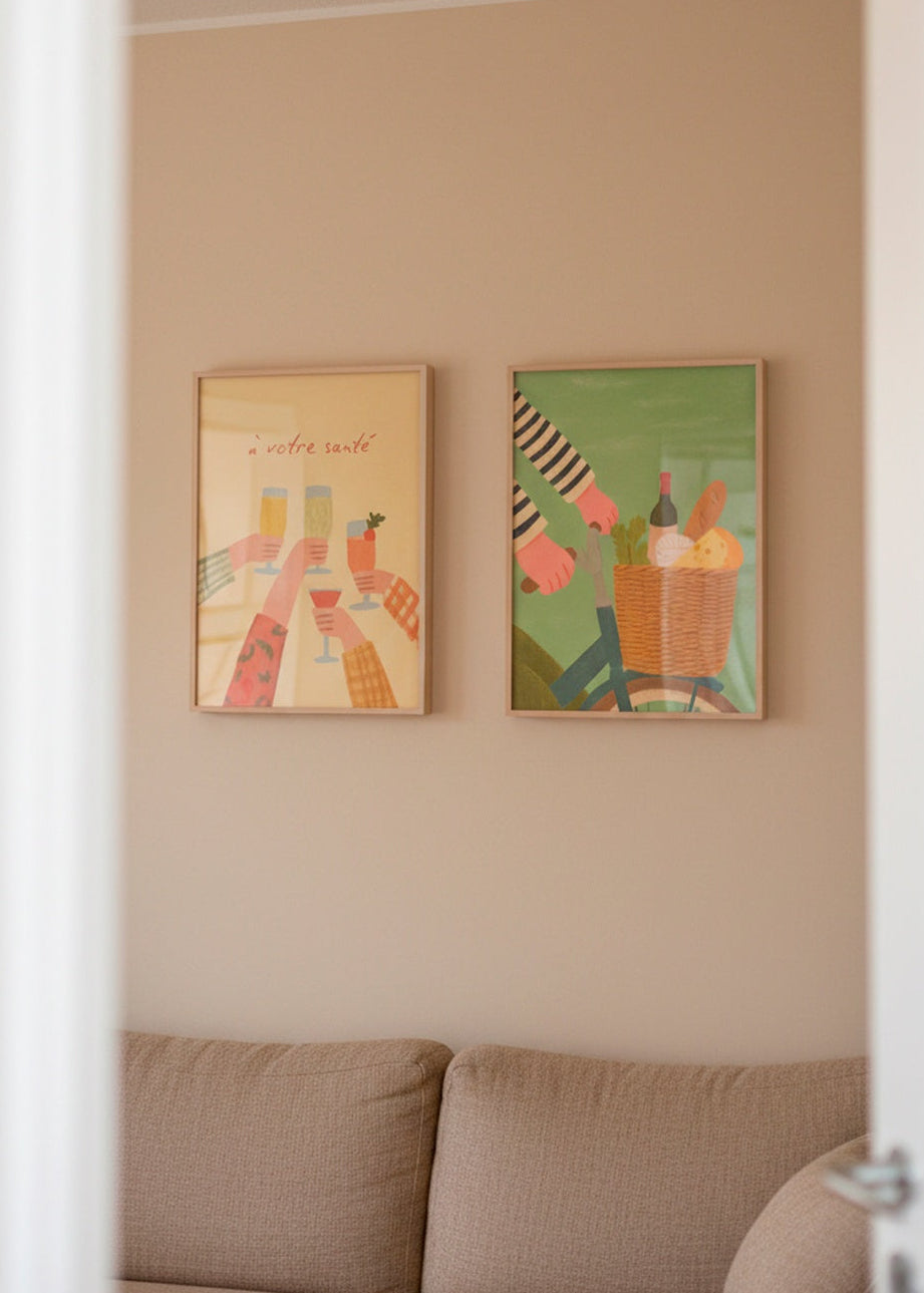 Two framed posters — “À votre santé” and “French Picnic” — hanging above a beige sofa in a warm, neutral living room.
