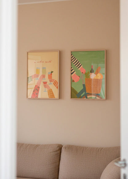 Two framed posters — “À votre santé” and “French Picnic” — hanging above a beige sofa in a warm, neutral living room.
