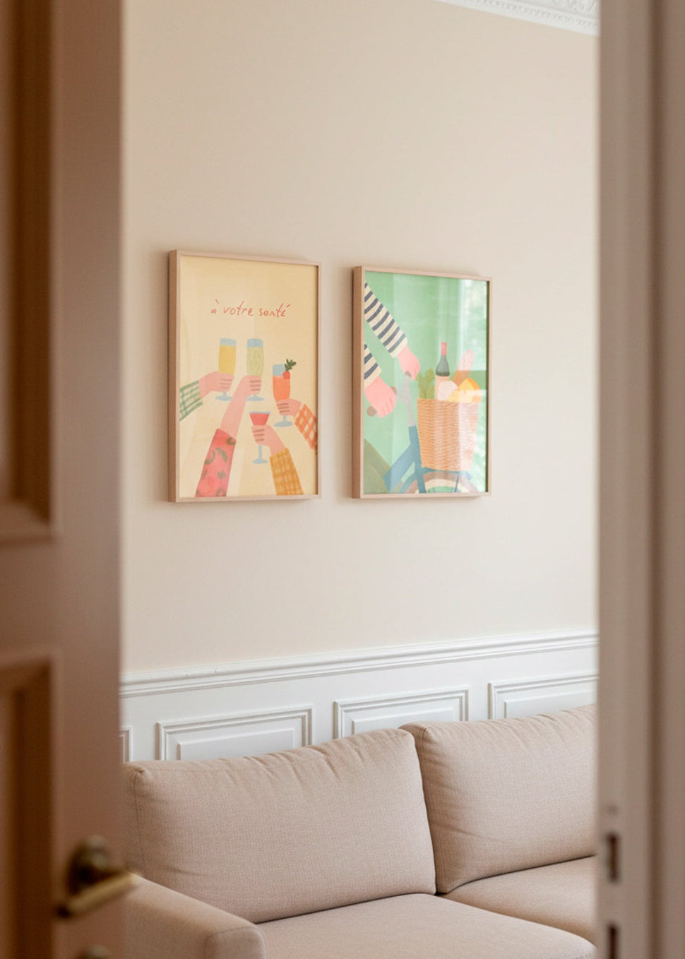Framed “À votre santé” and “French Picnic” posters on a beige wall with classic moulding above a light sofa.